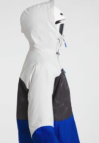 Skijack met een witte capuchon, zwarte en blauwe kleurblokken, gestructureerde patronen en felblauwe ritssluitingen. Glad materiaalafwerking.