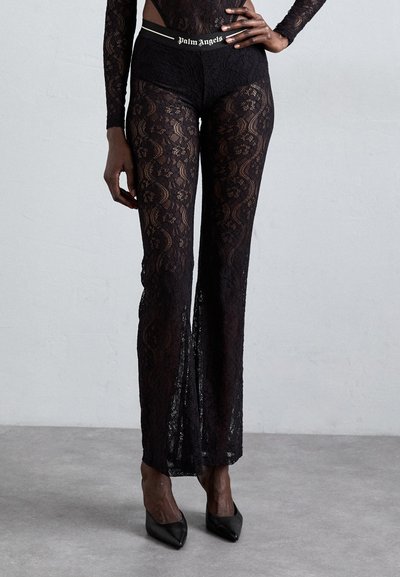 Pantalones de encaje negro con una cintura ajustada que presenta el logo de "Palm Angels". La tela tiene un patrón floral y se extiende hacia un diseño de pierna ancha.