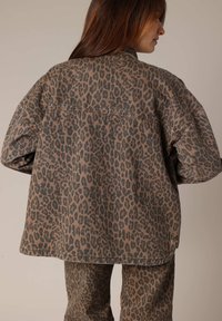 Veste en imprimé léopard marron et noir, coupe oversize, en denim, avec des coutures visibles, un dos uni et des manches amples.