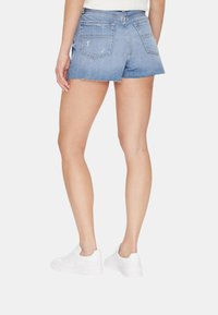 Shorts in denim, blu con orlo sfrangiato, dotati di due tasche posteriori e vita aderente, abbinati a sneaker bianche.