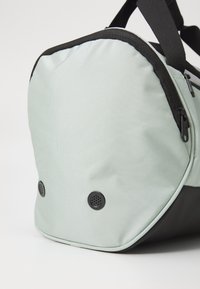 Svijetlo tirkizni ruksak s teksturiranom površinom, crnim detaljima i trakama, s dva okrugla otvora za ventilaciju blizu osnove.