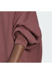 Ett arm rullat upp i en mauve långtärmad sweatshirt, som visar en del av underarmen mot en enkel ljus bakgrund.