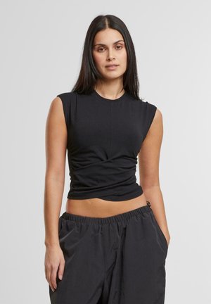 Haut noir sans manches au design ajusté et avec des détails froncés à la taille, fabriqué en tissu doux et extensible. Associé à un pantalon noir ample.