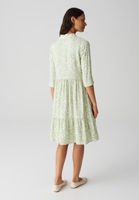 Robe à motifs verts et blancs avec des manches trois-quarts, taille cintrée et ourlet à volants. Tissu doux, silhouette évasée et design décontracté.