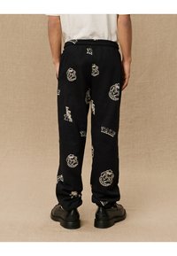 Svarte joggebukser med gjentatte Yale- og bulldoggrafikker i krem. Elastisk midje og avslappet passform, laget av myk stoff.