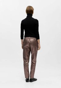 Metallisch bronze Hosen mit glänzender Textur, ausgestattet mit einem elastischen Bund und Gesäßtaschen, kombiniert mit einem figurbetonten schwarzen Rollkragenpullover.