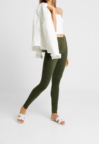 Gröna rutiga leggings i stretchtyg, hög midja med en slät yta. Matchas med en vit kort topp och en jeansjacka.