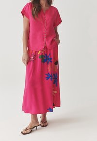 Lyserød skjorte med korte ærmer parret med en lang lyserød nederdel med multicolore blomster mønstre. Glat tekstur, casual pasform.