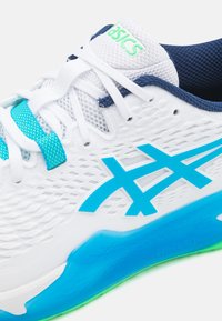 Hvide atletiksko med et blåt accent, mesh-overdel, teksturerede detaljer og en blå sål med grøn trim. ASICS-logo på tungen.