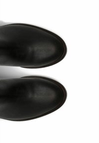 Botas de cuero negro hasta el tobillo con una textura suave, punta redondeada y una suela de perfil bajo que presenta costuras sutiles a lo largo de los bordes.