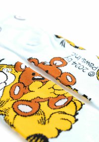 Calzini colorati con un design di cartone animato, base azzurro chiaro, personaggi orsi gialli e marroni, e contorni neri. Finitura tessile morbida.