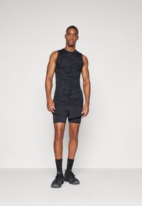 Svart ermeløs treningssinglet med camouflasjemønster, kombinert med svarte shorts. Materialet er glatt, tilpasset design, egnet for trening.