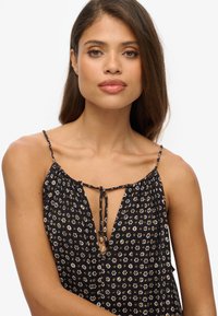 Zwarte bloemen top met dunne bandjes en een keyhole strikdetail bij de halslijn, met een klein bloemenpatroon en een zachte textuur.