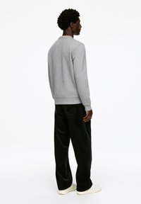 Gray sweatshirt with a crew neckline, ribbed cuffs, and hem, paired with black corduroy pants. Model faces away, showcasing the back view.