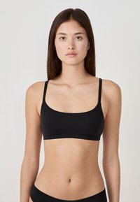 Zwarte bralette met dunne bandjes, een soepele textuur en een ronde halslijn. Eenvoudig ontwerp, zonder sluitingen of versieringen.