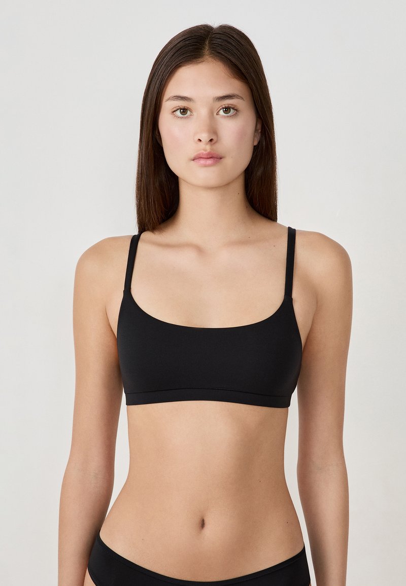 Zwarte bralette met dunne bandjes, een soepele textuur en een ronde halslijn. Eenvoudig ontwerp, zonder sluitingen of versieringen.