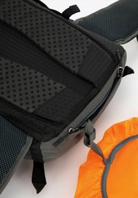 Sac à dos noir et gris avec un tissu texturé, un rembourrage en maille et une fermeture éclair. Un accessoire rond orange est à proximité, avec un bord en gathering.