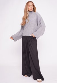 Jasnoszary, oversize sweter z wysokim kołnierzem i szerokimi rękawami, zestawiony z luźnymi czarnymi spodniami z plisami z przodu. Strukturalny materiał dzianinowy.