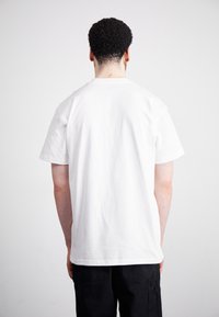 T-shirt bianca in cotone con maniche corte, collo rotondo e orlo dritto, vista dal retro, che mostra una superficie liscia.