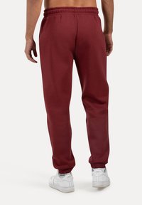 Bordeaux kleurige sweatpants met een elastische tailleband en opgerolde pijpen, gemaakt van een zachte, gestructureerde stof. Witte sneakers maken de outfit compleet.