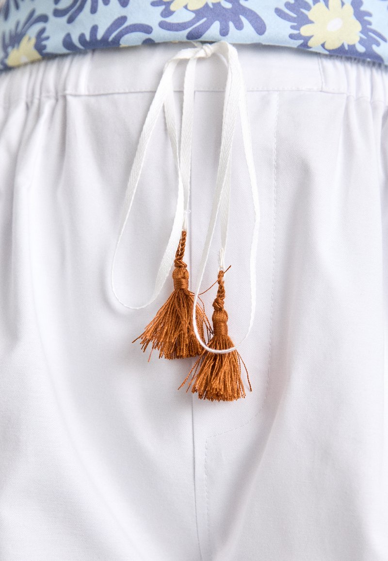 White pants with an elastic waistband, featuring two white drawstrings ending in brown tassels. The design includes a smooth texture.