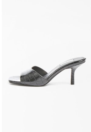 Mules negros de tacón con un patrón de cocodrilo. Diseño de punta abierta, acabado suave y un tacón delgado de 3 pulgadas. Silueta elegante y minimalista.