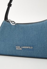 Bolsa de denim azul com alça preta, fecho de correr prateado e logótipo "KARL LAGERFELD JEANS" em letras metálicas na parte frontal.
