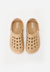 Tan rubber clogs with a molded design, featuring multiple round ventilation holes and an adjustable heel strap for a secure fit.