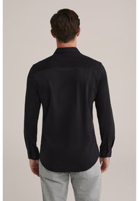 Juoda, ilgomis rankovėmis marškinėliai su apykakle, sagomis užsegamais rankogaliais ir šiek tiek išlenkta apačia. Audinys atrodo lygus, vientisos tekstūros.