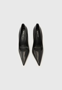 Par svartspissede Michael Kors høyhælte skinnsko sett ovenfra på en lys bakgrunn.