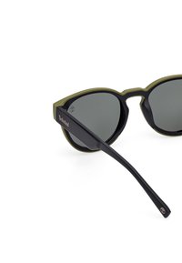 Gafas de sol con montura negra y verde oliva. Lentes gris oscuro, con forma de ojos de gato mediana. Logotipo de Timberland destacado en la patilla.