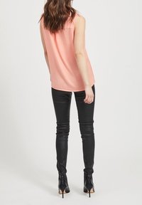 Haut sans manches de couleur pêche clair avec une coupe décontractée, associé à un pantalon en cuir noir moulant et des bottines noires à talons hauts. Design simple.