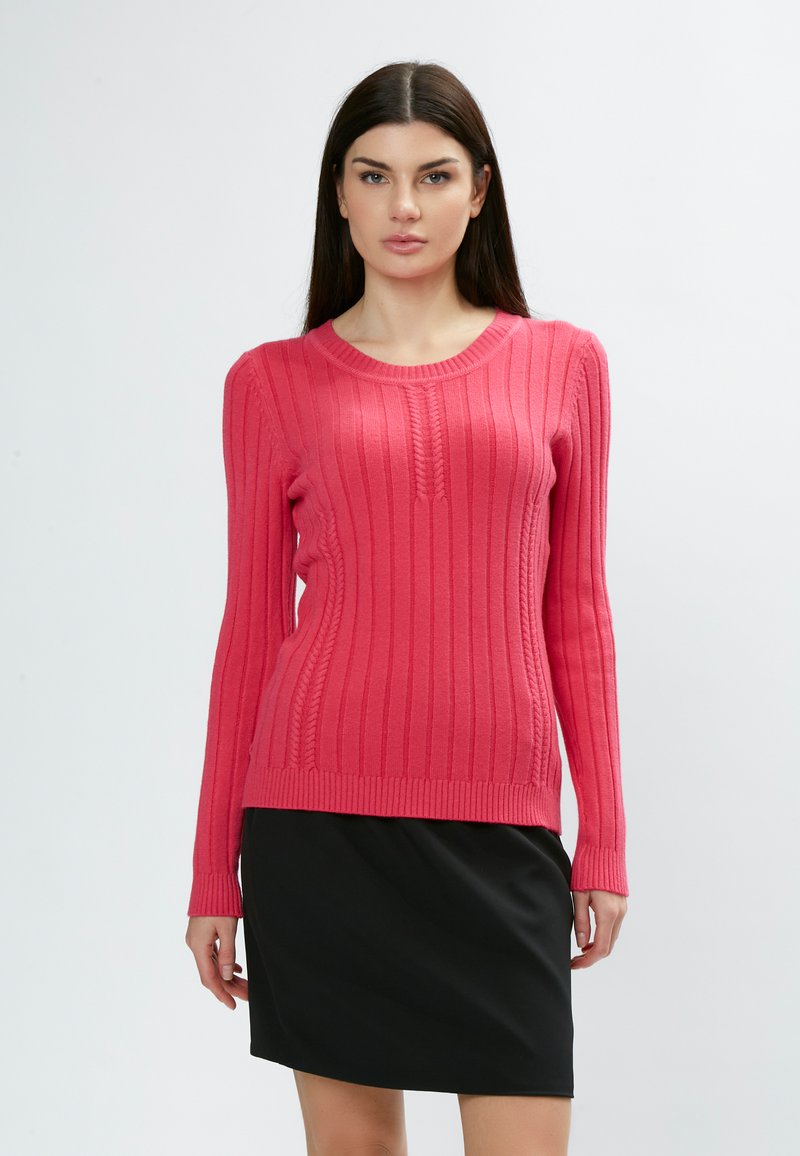 Maglione rosa a coste con maniche lunghe e scollatura a girocollo, caratterizzato da linee verticali testurizzate e un design aderente. Abbinato a una gonna nera.