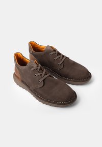 Zapatos de cuero marrón con un acabado texturizado, que presentan una puntera redonda, diseño de cordones y acentos naranjas en el interior. Detalle de suela cosida.