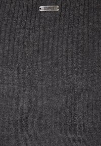 Mörkgrå ribbade stickade tröjfabriken med en metallisk silveretikett med "ESPRIT" präglad. Texturerad yta tillför djup.