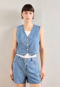 Denim prsluk s uzorkom dijamanta, prednjim gumbima i skraćenim dizajnom, uparen s odgovarajućim trapericama. Svijetloplava boja s bijelim akcentima.