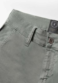 Lichtgrijze broek met een gladde textuur, voorzien van een knoopsluiting, riemlussen en een label op de tailleband. Gestikte details zijn zichtbaar.