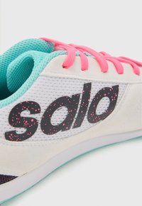 Vit sneakers med mesh-design, rosa snören och "sala"-logotyp i svart med rosa prickar. Aqua-accenter på det inre fodret och sulan.
