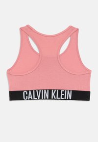 Rosa racerback sportbh med svart band i botten som har en vit Calvin Klein-logotyp, placerad liggande på vit bakgrund.