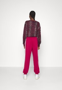 Sweatshirt med leopardmönster och långa ärmar, matchad med rosa joggers med vita sidestreck och elastisk midja.