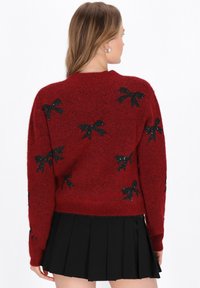 Röd fluffig tröja med svarta paljettb�ågar, långa ärmar och rundad halsringning, kombinerad med en svart plisserad kjol.