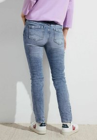 Jeans en denim bleu ajustés avec un délavage, comportant deux poches arrière et une texture lisse. Associés à des baskets blanches.