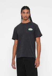 Sort bomulds t-shirt med korte ærmer, rund halsudskæring og et farverigt grafisk logo på venstre brystområde. Enkel og afslappet design.
