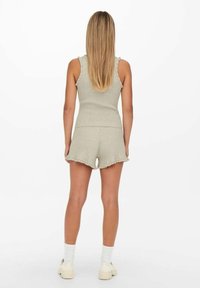 Conjunto de dos piezas gris claro con textura acanalada que incluye una camiseta sin mangas con bordes con volante y pantalones cortos con dobladillo deshilachado. Se lleva con calcetines blancos hasta el medio y zapatillas deportivas.