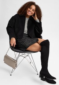 Zwarte wol blend jas, grijze trui, leren rok, zwarte suede over-de-knie laarzen met blokhakken en een metallic clutch tas.