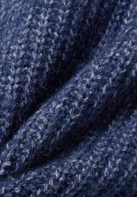 Close-up van zacht marineblauw gebreid stof met een gestructureerd, pluizig garen en zichtbare breisteken.