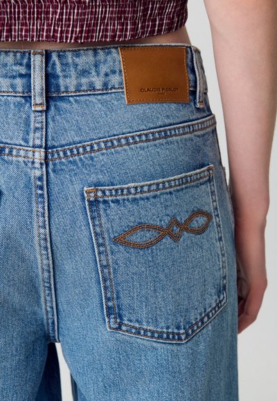 Jeans de mezclilla azul claro con una etiqueta de cuero marrón en la cintura y un patrón decorativo bordado en el bolsillo trasero.