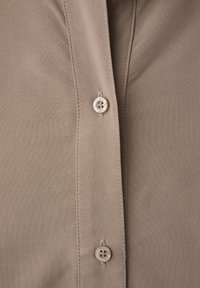 Primo piano di tessuto beige con due bottoni perlati e cuciture visibili lungo la patta dei bottoni.