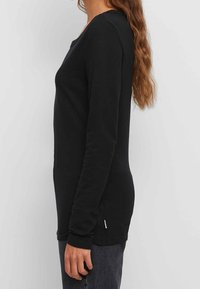 Zwarte lange mouwen shirt met een ronde hals en een hoge-achter lage-voor broek, gemaakt van zachte stof. Heeft aangesloten mouwen en subtiele zijdetails.