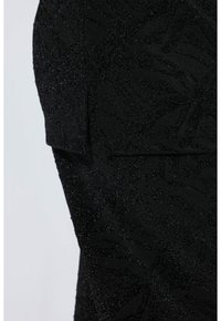 Černá texturovaná tkanina s motivem listů a jemným leskem. Hladký povrch s detailním vzorem. Přiblížení boční části oděvu.